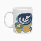 Latte art tulip in a small glass cup, on a white ceramic mug. The design includes 3 of that same pour in different sizes printed on each side of the mug. Main colors: green, blue, brown, mustard-yellow